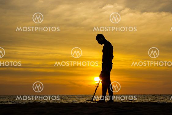Treasure hunter with Metal detector on the sunset the beach
