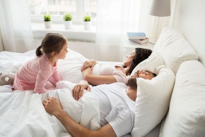 little girl waking her sleeping parents up in bed