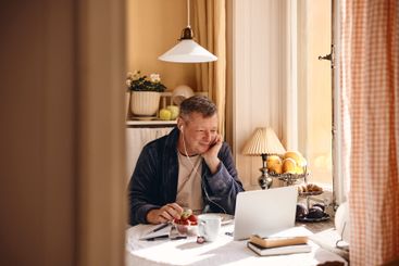 Smiling man with wired in-ear headphones watching laptop...