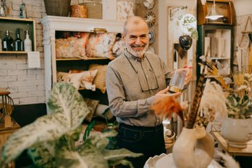 Happy senior male owner showing glass decor at home...