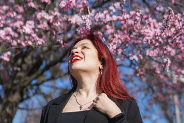 Red haired woman wearing stylish outfit near blossoming...