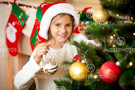 cute smiling girl decorating Christmas tree with golden...