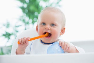 Baby looking at camera while holding a plastic spoon