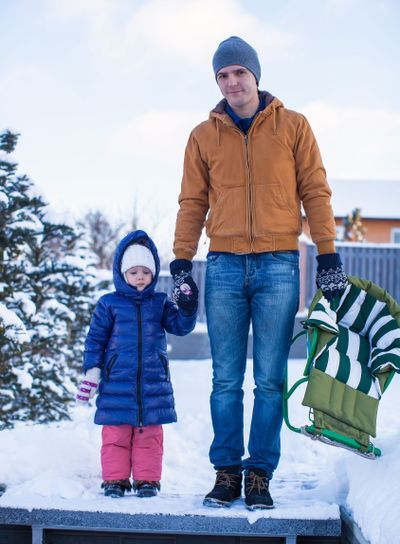Young dad and little girl go sledding in a cold winter day