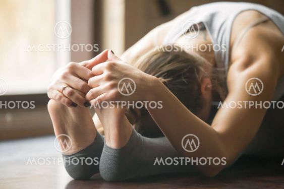 Young woman in paschimottanasana pose, home interior background,
