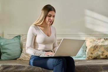 Young woman working at home, sitting on couch using laptop