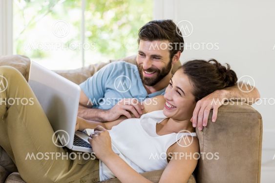 Happy couple lying on sofa and using laptop
