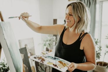 Happy woman, painting in workshop with palette and...