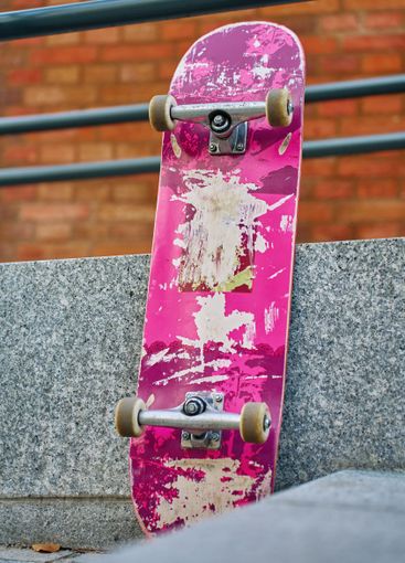 Used pink skateboard against stone wall in urban setting