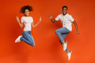 Excited black couple jumping on orange background