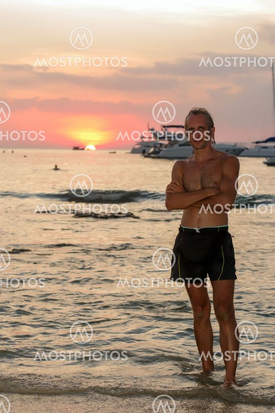 colorfull portrait of handsome topless man looking up and smiling during sunset at the beach.