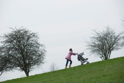Mother Pushing Stroller Uphill In Park