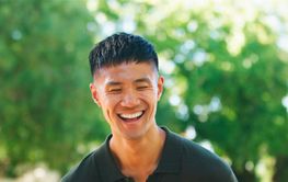 Young Man Laughing Outdoors in a Sunlit Park During a...