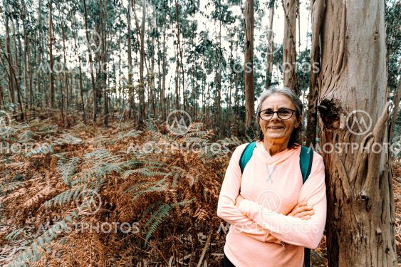 Old woman leaning on a tree while smiling to camera in...