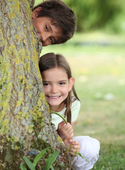 Two little children hiding behind tree
