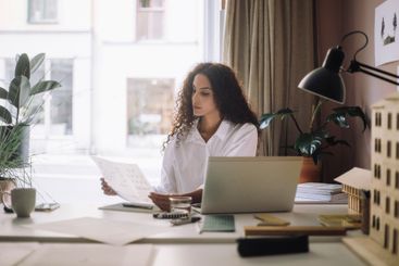 Female design professional examining blueprints while...