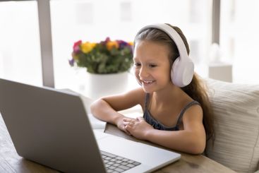 Little girl listens audio lesson through headphones,...