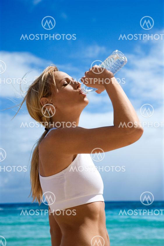 Woman drinking water on beach.