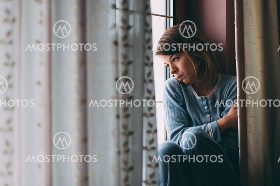 Young sad woman sitting on the window