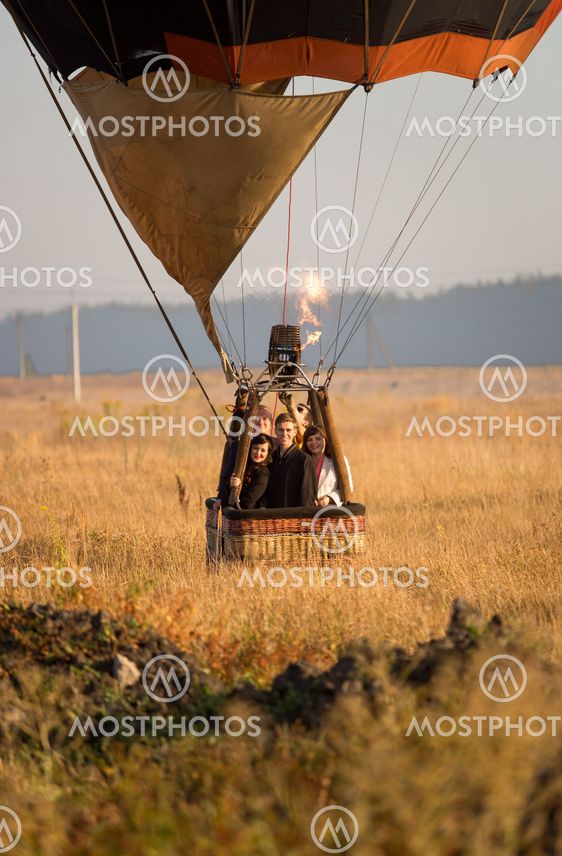Take off of hot air balloon with crew at field at sunrise