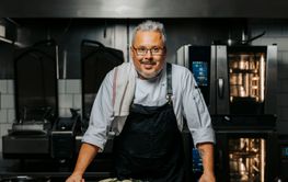 Portrait of smiling mature male chef wearing apron and standing in kitchen at restaurant