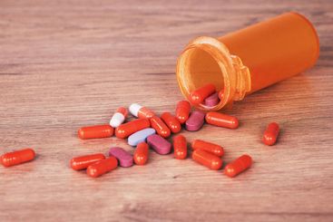 An open orange bottle of brightly coloured pills spilled...