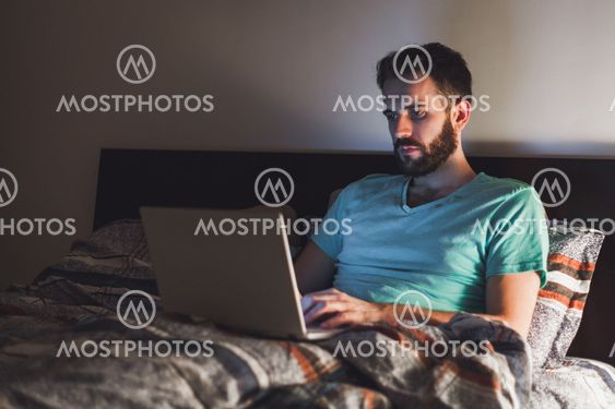 Young man working late in bed on a laptop