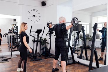 Elderly man in ems suit is training with personal...