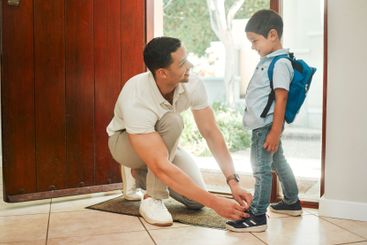 Happy father, tying shoes and school with son by door...