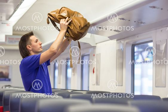 Young caucasian man putting luggage on the top shelf at...