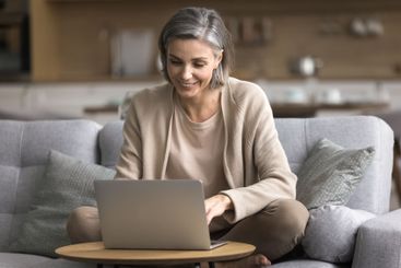 Confident aged woman working on notebook at home office...