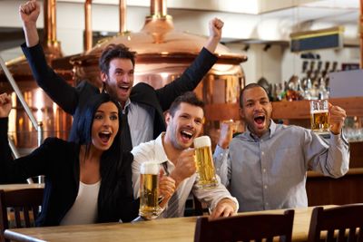 Happy fans watching TV in pub cheering�