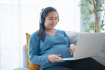 Pregnant asian woman using laptop  sitting on sofa at...