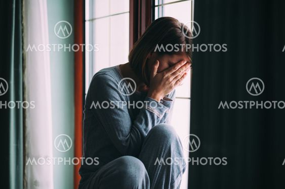 Young sad woman sitting on the window