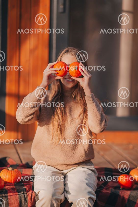 Beautiful girl covered her eyes with pumpkins at autumn...