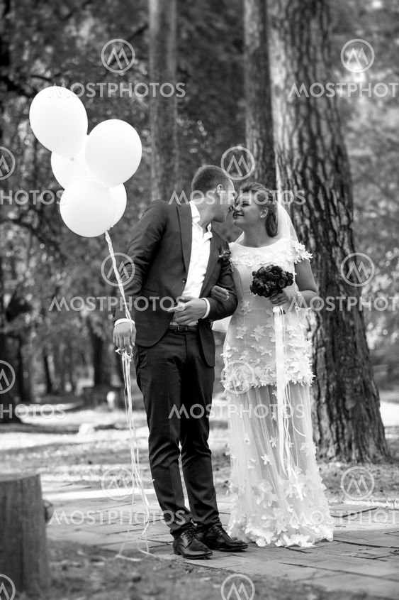 groom holding balloons kissing beautiful bride at park