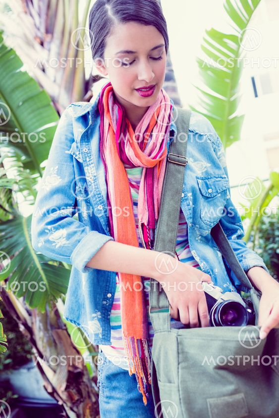 Young smiling woman taking camera out from her bag outside