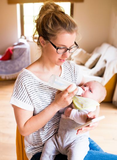 Beautiful mother feeding baby son, milk in bottle,...