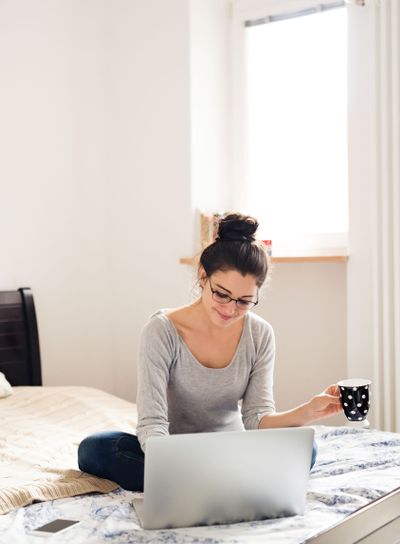 Beautiful young woman sitting on bed, working. Home office.