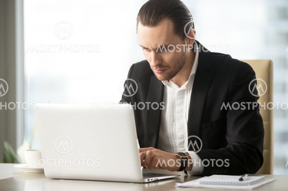 Serious young businessman working on laptop at work in office.