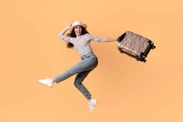 Cheerful Young Female Traveller Jumping With Suitcase In...