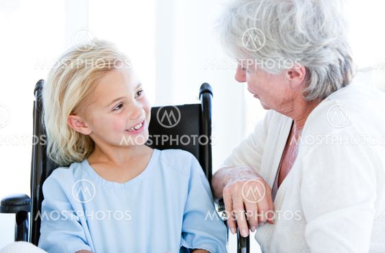 Cute little girl sitting on a wheelchair talking with her grandmother