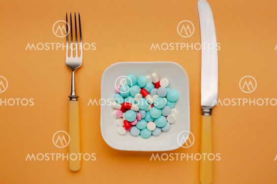 White plate with different pills on it with knife and fork