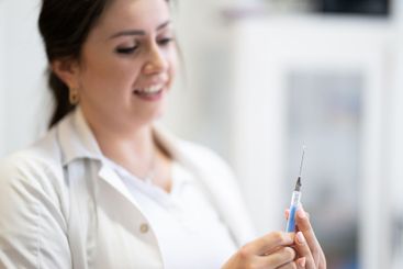 A focused nurse in a white lab coat carefully prepares a...