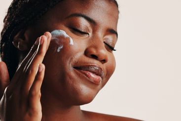 Happy, black woman and lotion on face in studio for...