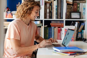 Happy curly man indoors at home using laptop computer
