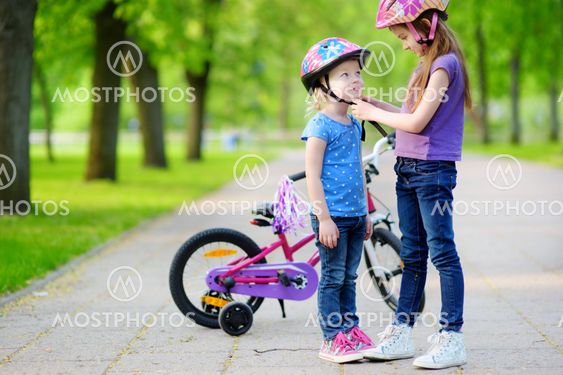 Adorable girl helping her sister to put a bicycle helmet on