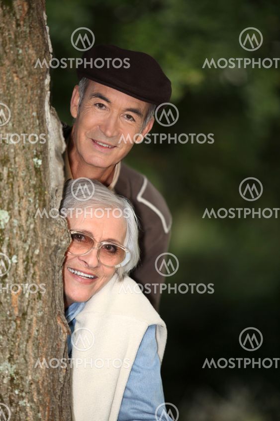 Elderly couple hiding behind a tree
