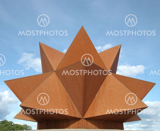 Rostig geometri mot blå, men molnig himmel.