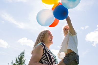 Mother And Daughter Playing With Balloons Against Sky